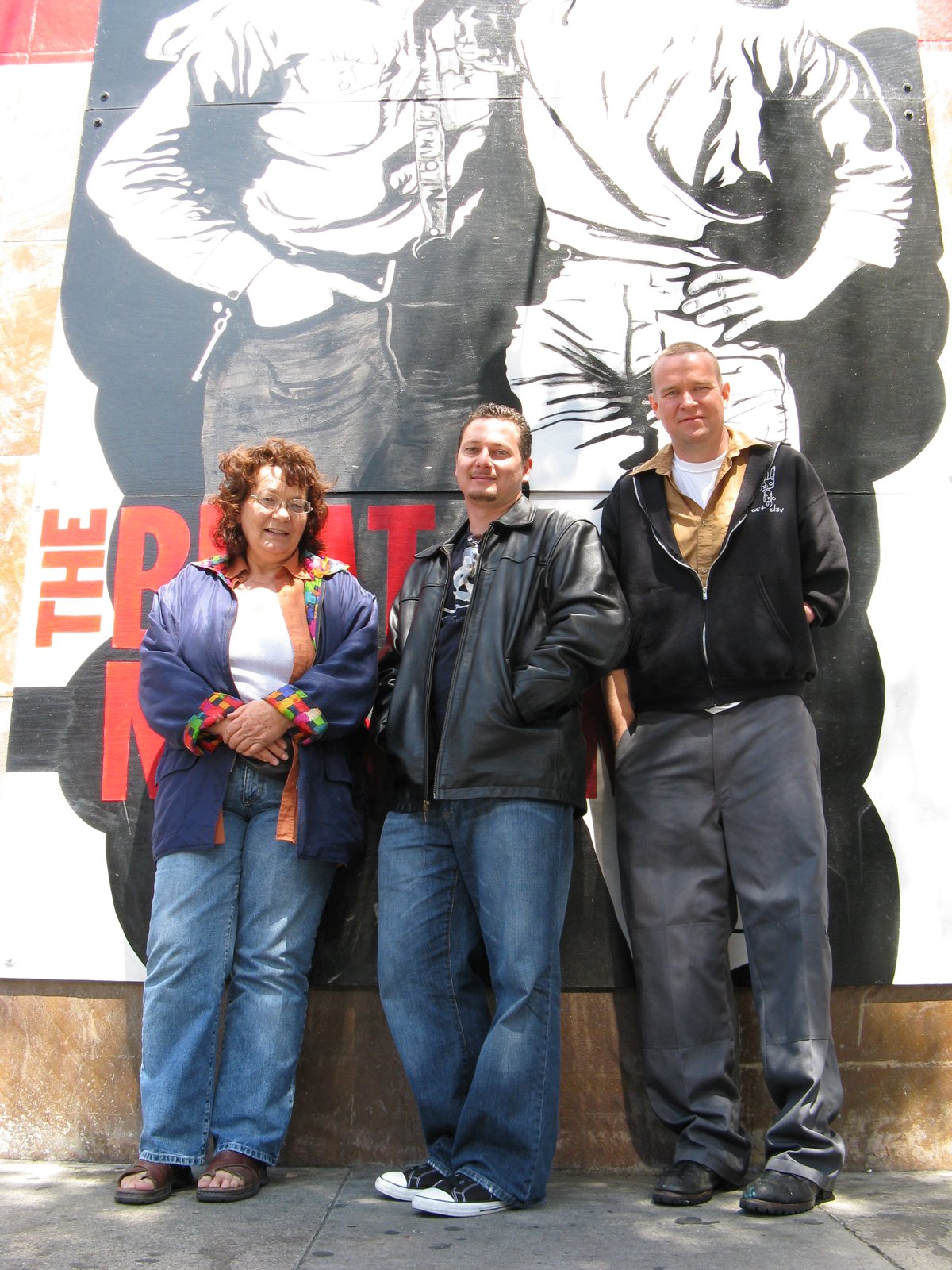 Three people standing beneath a large black-and-white mural at The Beat Museum