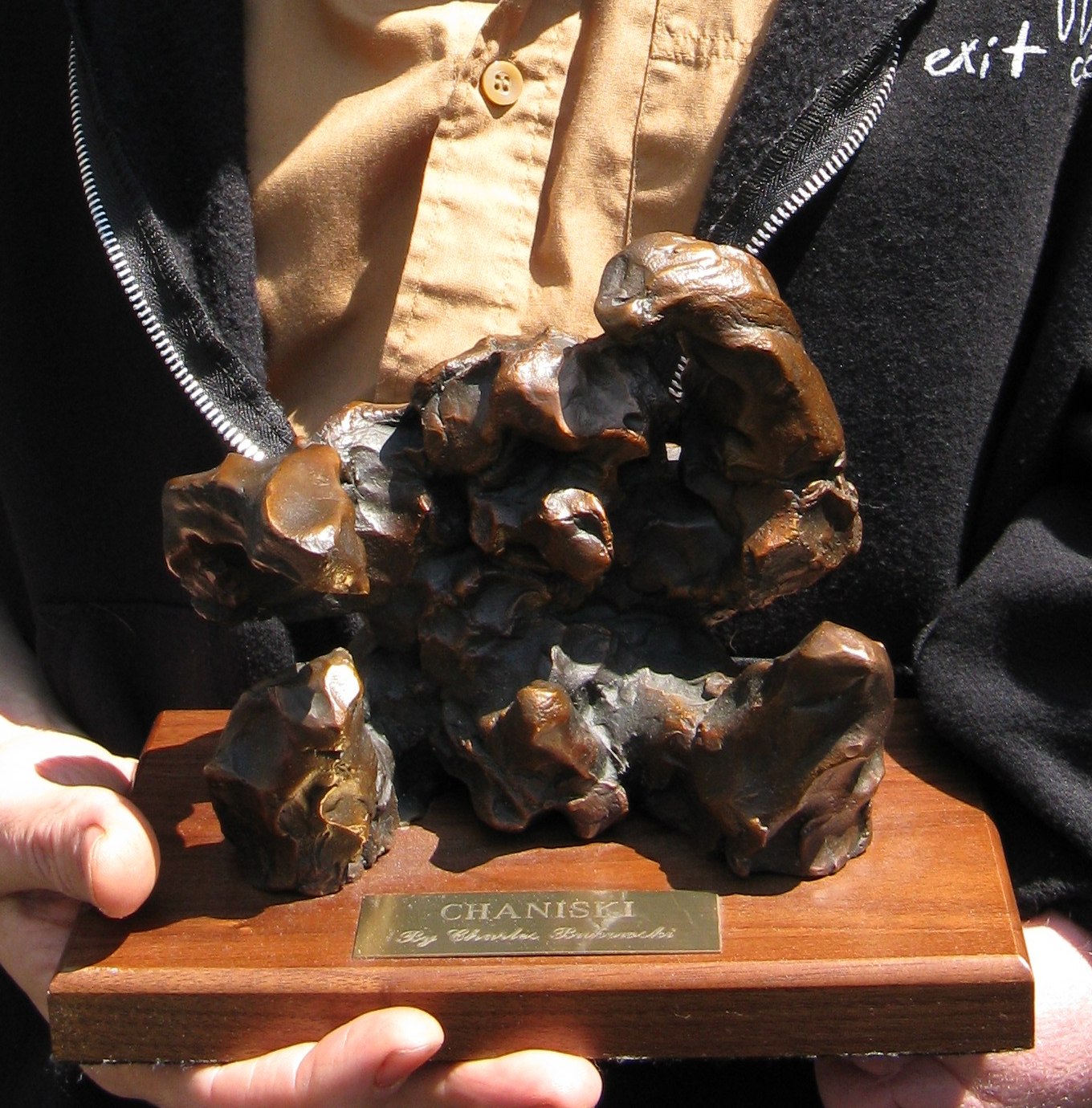 Small, craggy dark bronze sculpture on a walnut base, held in two hands; the brass plate reads CHANISKI, By Charles Bukowski