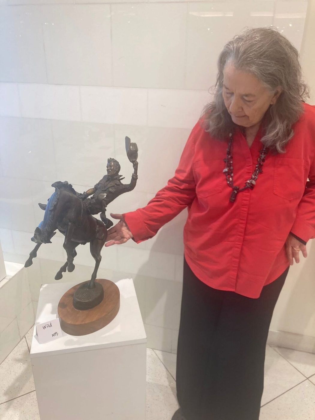 Linda King beside a bronze of a rider on a bucking horse